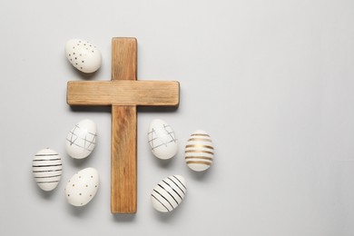 Photo of Wooden cross and painted Easter eggs on light grey background, flat lay. Space for text