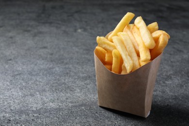 Photo of Delicious french fries in paper box on grey table, closeup. Space for text