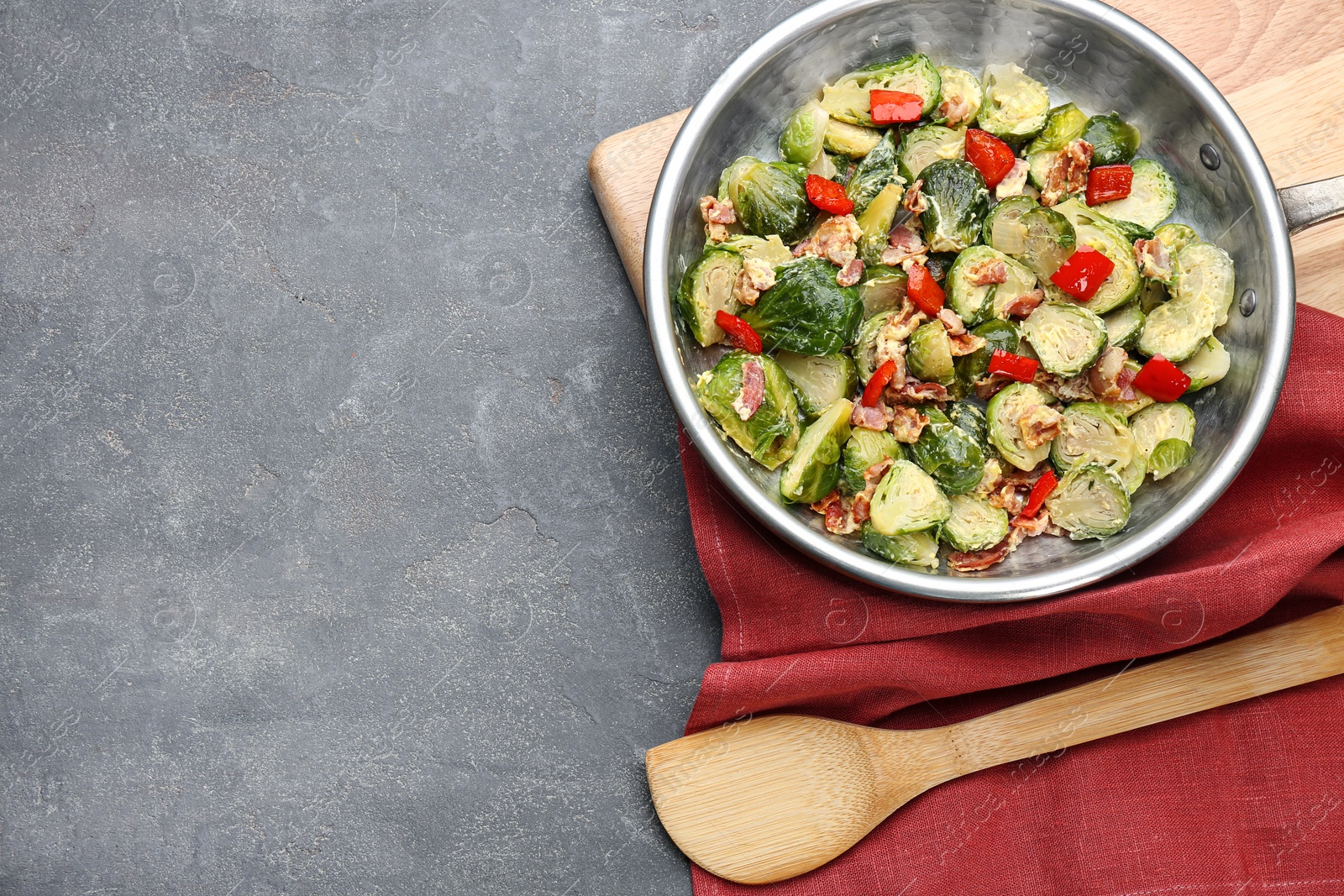 Photo of Delicious Brussels sprouts with bacon in pan on grey table, top view. Space for text