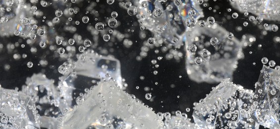 Soda water with ice cubes against dark background, closeup. Banner design