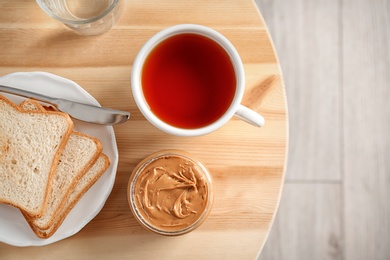 Photo of Jar of creamy peanut butter with bread and cup of tea on table