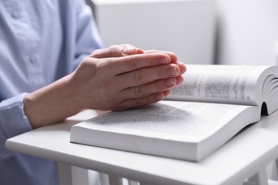 Photo of Religion. Christian woman praying over Bible indoors, closeup