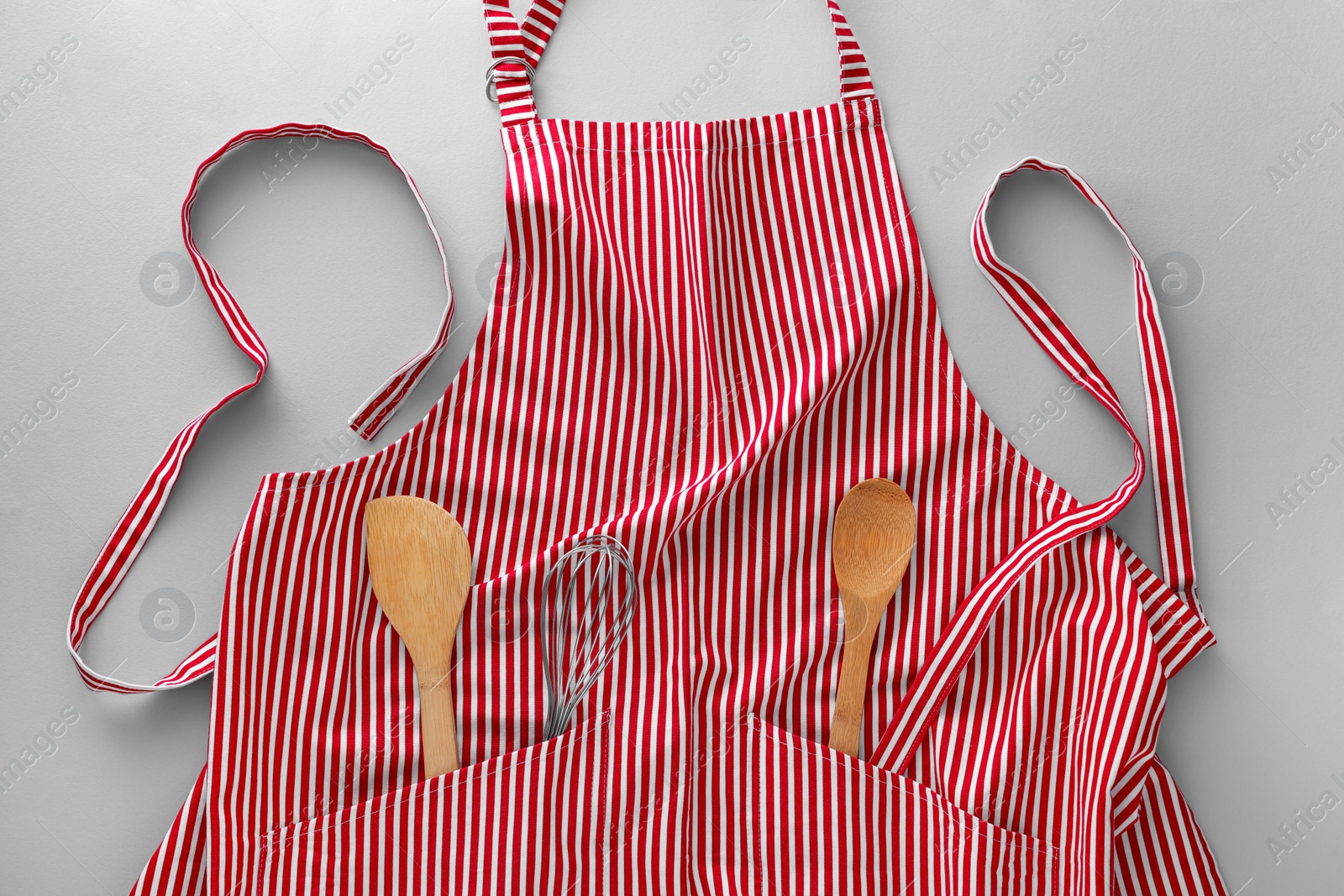 Photo of Red striped apron with kitchen tools on light grey background, top view