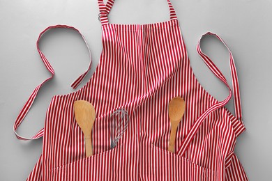 Red striped apron with kitchen tools on light grey background, top view