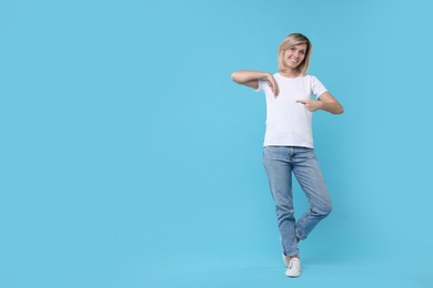 Happy woman pointing on light blue background, space for text