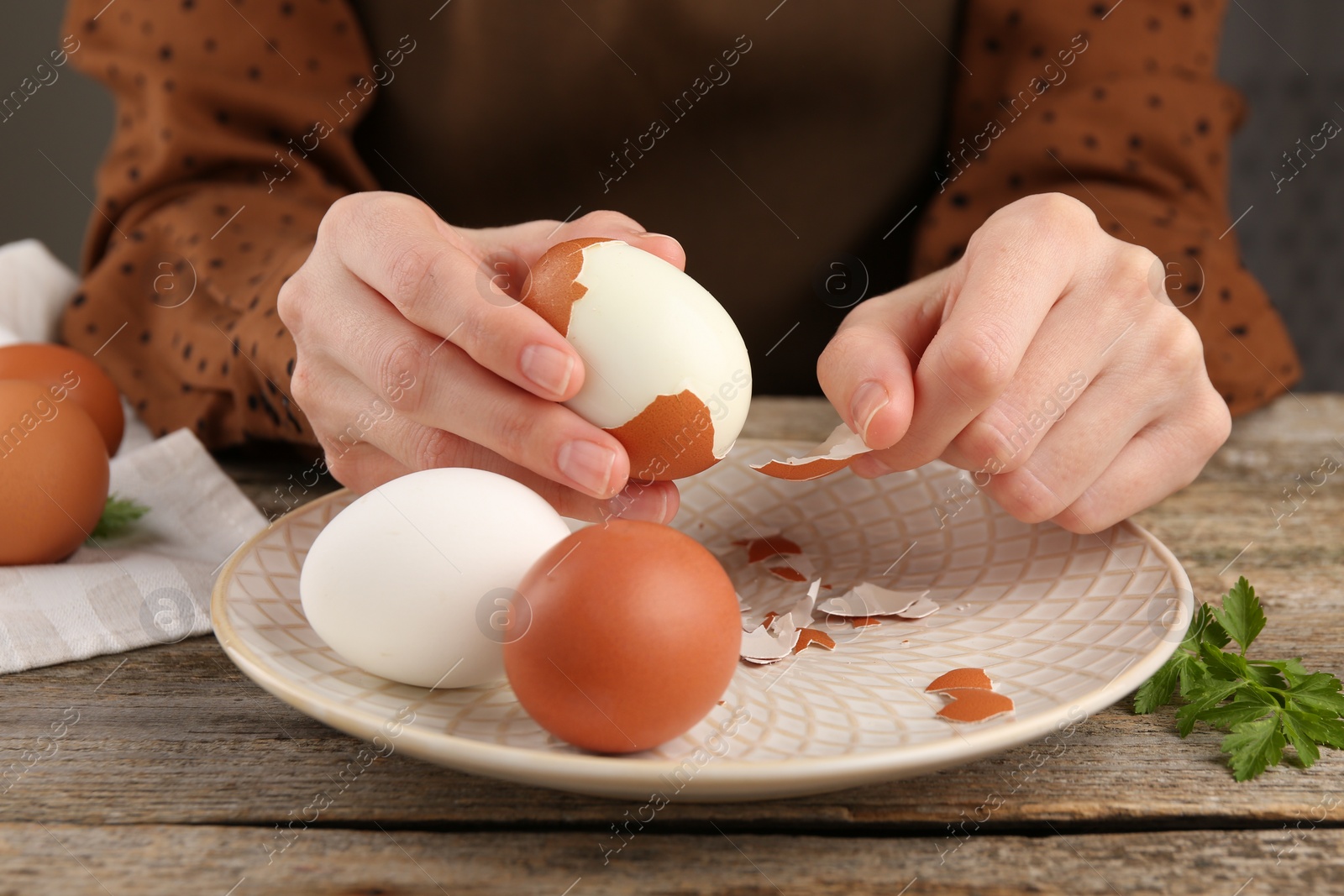 Photo of Woman peeling boiled egg at old wooden table, closeup