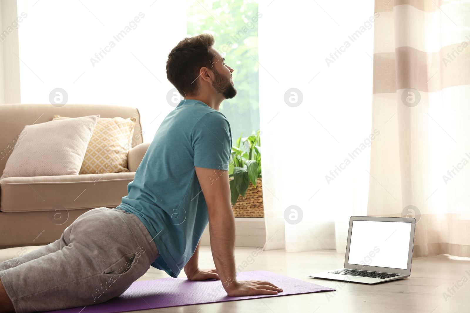 Photo of Man practicing yoga while watching online class at home during coronavirus pandemic. Social distancing