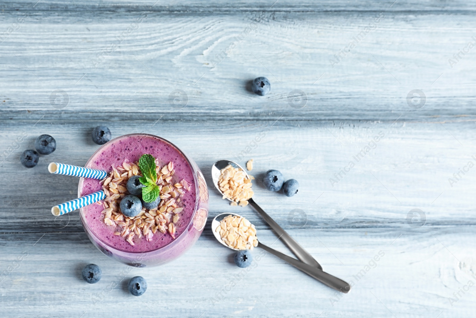 Photo of Tasty blueberry smoothie in glass, berries, oatmeal and space for text on wooden table, top view