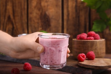 Woman holding glass of tasty raspberry smoothie over wooden table, closeup