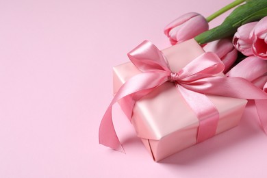 Beautiful gift box with bow and tulip flowers on pink background, closeup. Space for text
