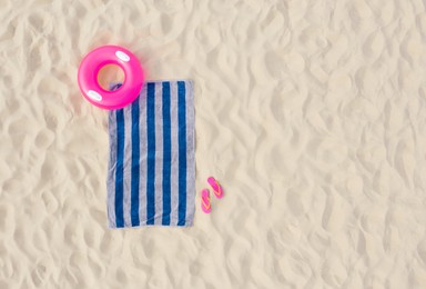 Image of Striped beach towel, flip flops and swim ring on sand, aerial view. Space for text