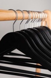 Photo of Black clothes hangers on wooden rail against light grey background, closeup