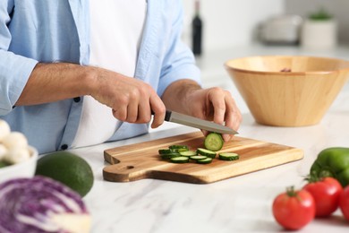 Photo of Man cutting cucumber at table in kitchen, closeup. Online cooking course