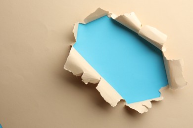 Photo of Hole in beige paper on light blue background, space for text