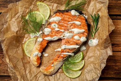 Photo of Tasty salmon steak with sauce, citrus slices and herbs on wooden table, top view