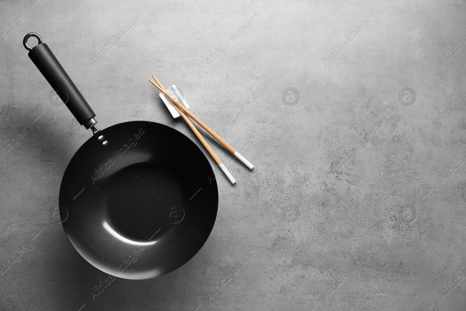 Photo of Empty wok and chopsticks on grey table, flat lay. Space for text