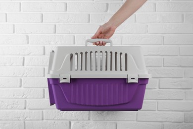 Photo of Woman holding violet pet carrier near white brick wall, closeup