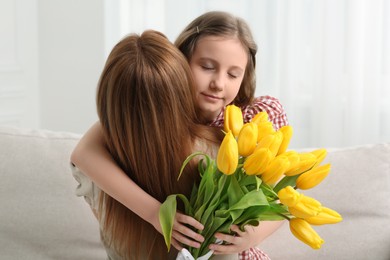 Daughter congratulating mom with bouquet of yellow tulips at home
