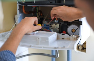 Photo of Man repairing gas boiler with screwdriver, closeup