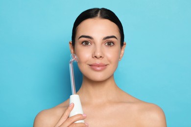 Photo of Woman using high frequency darsonval device on light blue background