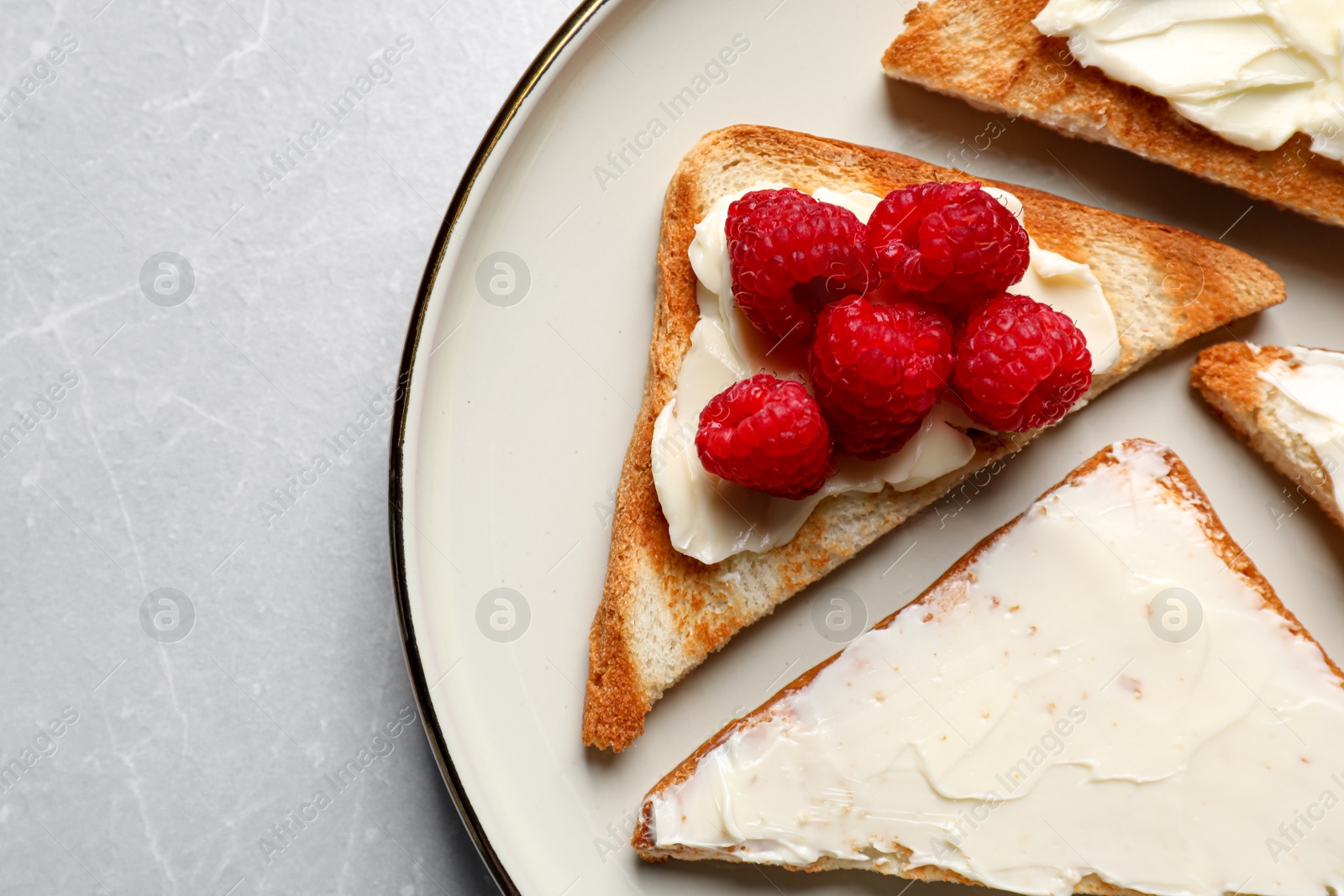 Photo of Tasty toasts with butter and raspberries on light grey marble table, top view