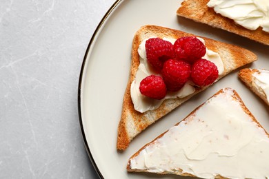 Photo of Tasty toasts with butter and raspberries on light grey marble table, top view