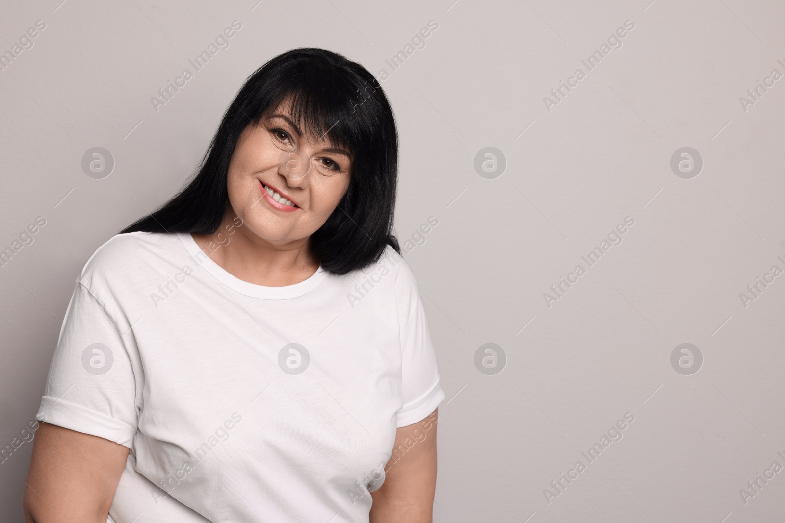 Photo of Beautiful overweight mature woman with charming smile on light grey background. Space for text