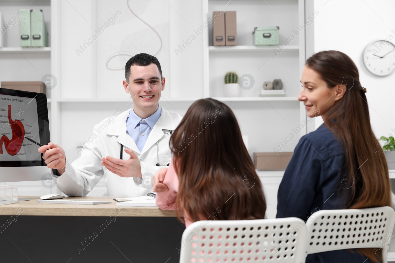 Photo of Gastroenterologist consulting woman with her daughter and showing image of stomach on computer in clinic