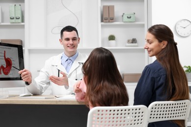 Gastroenterologist consulting woman with her daughter and showing image of stomach on computer in clinic