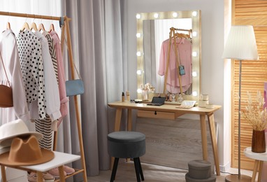 Makeup room. Stylish dressing table with mirror, chair and clothes rack indoors