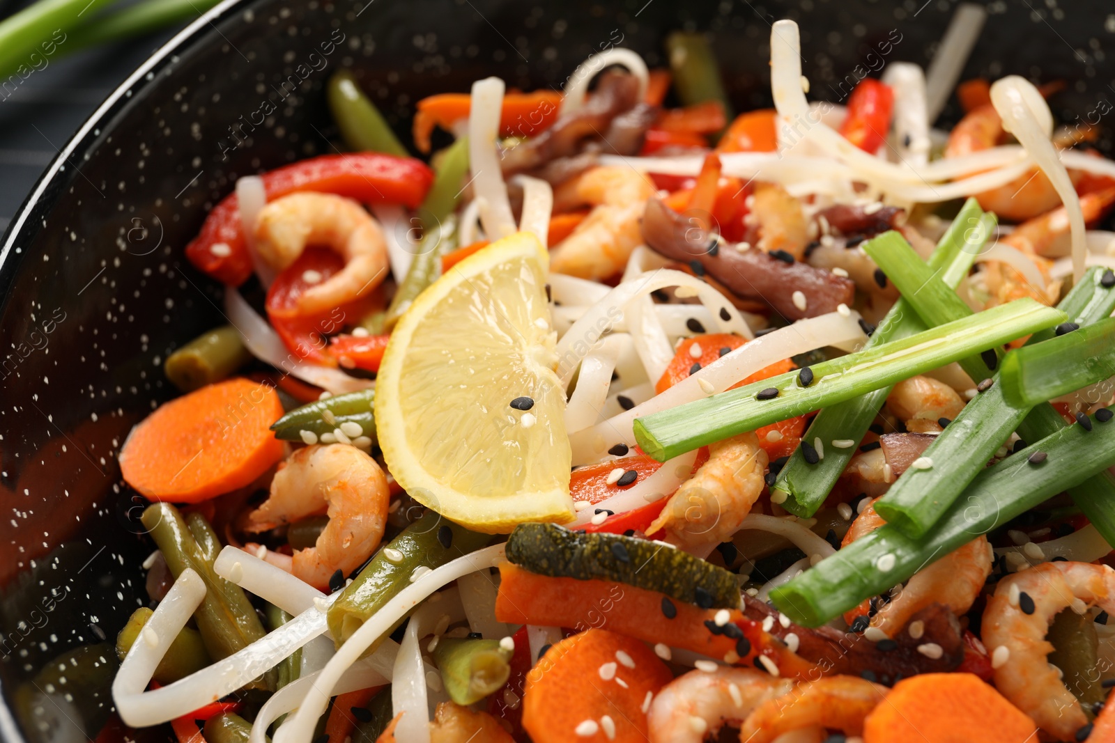 Photo of Shrimp stir fry with noodles and vegetables in wok, closeup