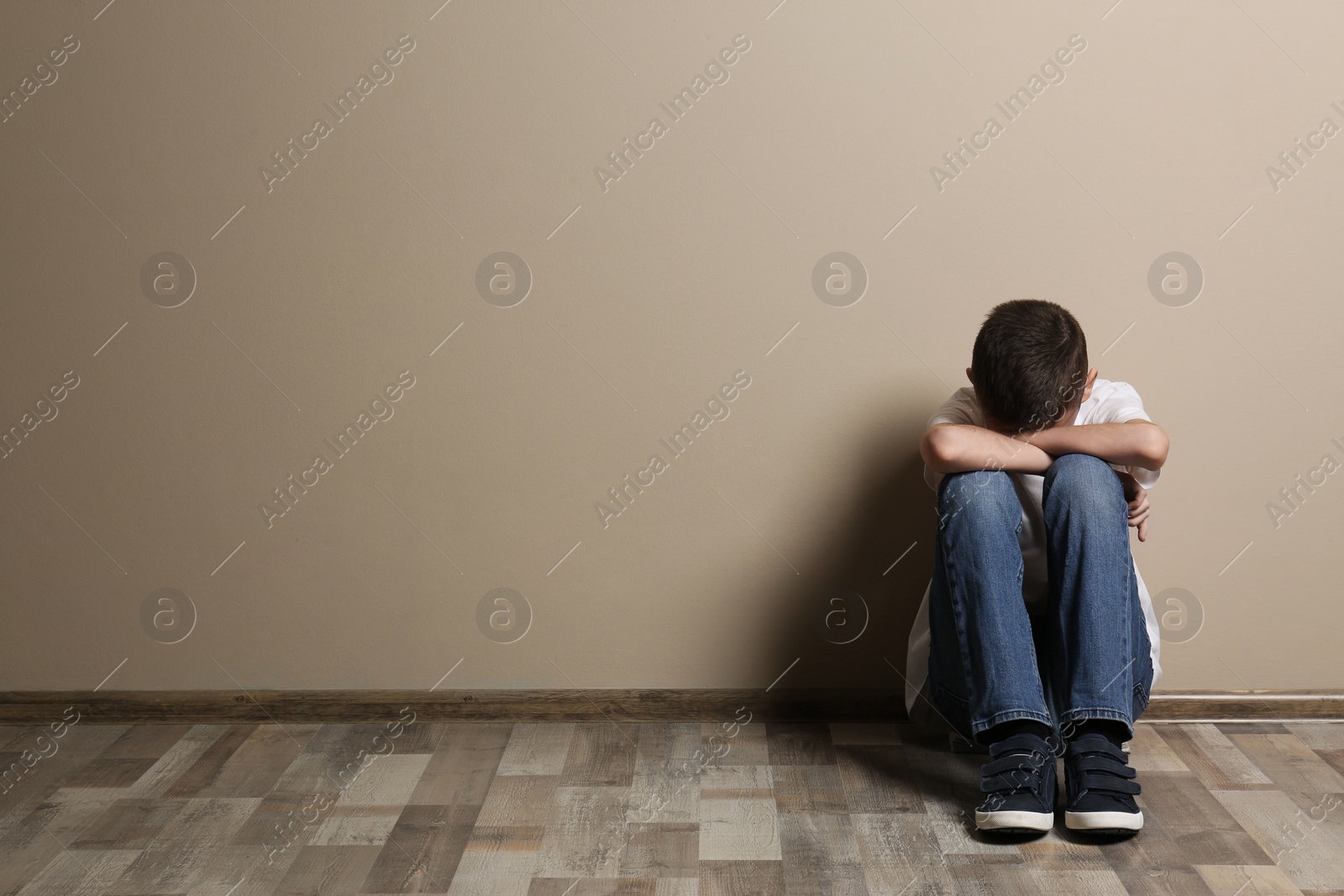 Photo of Upset boy sitting on floor at color wall. Space for text