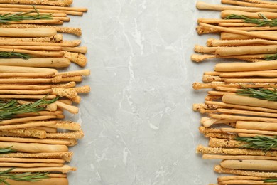 Delicious grissini sticks and rosemary on grey marble table, flat lay. Space for text