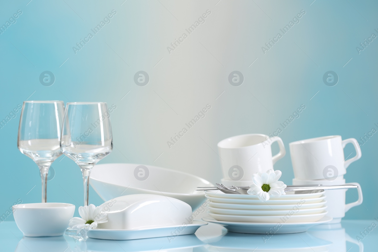 Photo of Set of many clean dishware, cutlery, flowers and glasses on light blue table