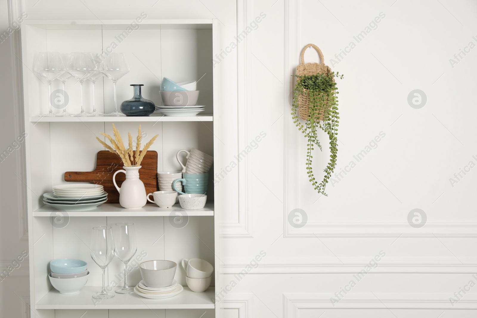 Photo of Different clean dishware and glasses on shelves in cabinet indoors