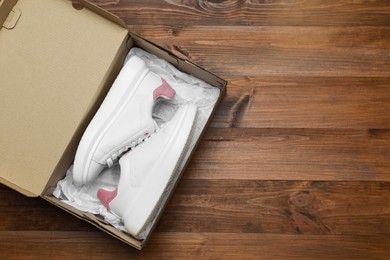 Photo of Pair of stylish sport shoes in cardboard box on wooden background, top view. Space for text