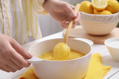 Woman cooking lemon curd at white wooden table, closeup