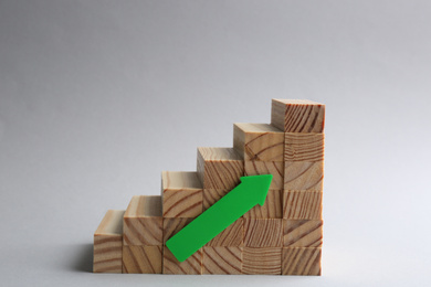 Photo of Stairs made of wooden blocks with green arrow on light grey background. Career promotion concept