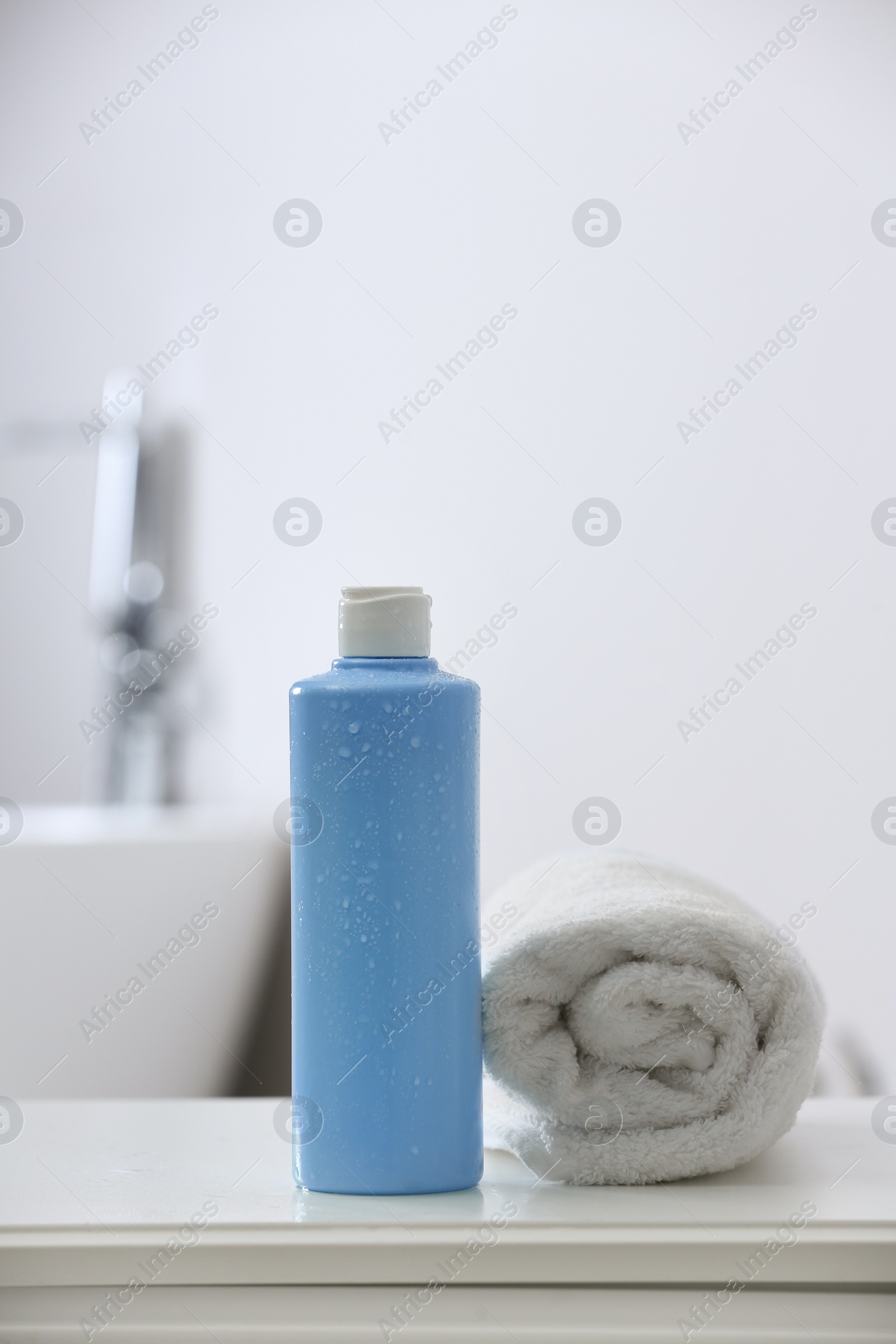 Photo of Bottle of bubble bath and towel on white table in bathroom