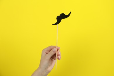 Photo of Woman with fake paper mustache on yellow background, closeup