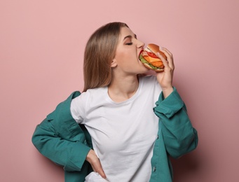 Pretty woman eating tasty burger on color background. Space for text