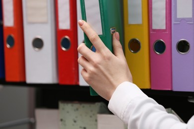 Photo of Woman taking folder with documents from shelf in office, closeup