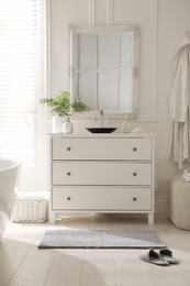 Stylish grey mat and slippers near chest of drawers in bathroom