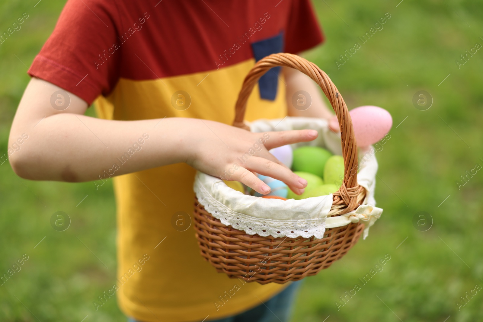 Photo of Easter celebration. Little boy holding basket with painted eggs outdoors, closeup