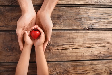 Photo of Family holding small red heart in hands on wooden background