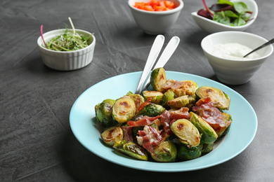 Photo of Delicious roasted Brussels sprouts with bacon served on black table