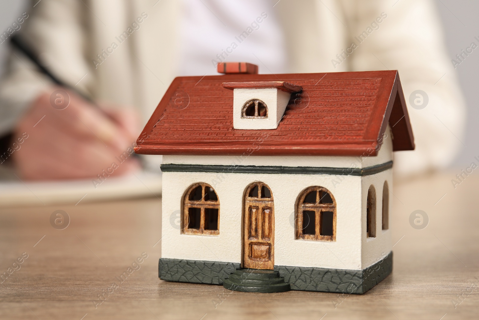 Photo of Mortgage concept. Woman writing at wooden table, focus on house model. Space for text