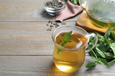 Photo of Cup with hot aromatic mint tea on wooden table, space for text