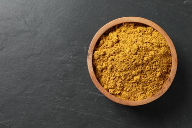 Dry curry powder in bowl on dark textured table, top view. Space for text