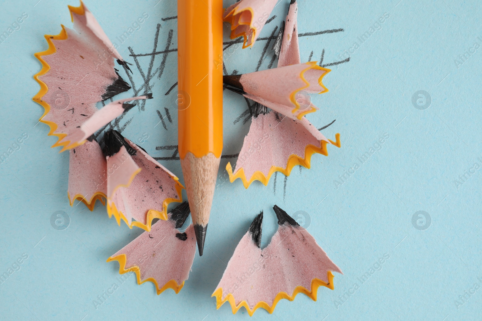 Photo of One sharp graphite pencil and shavings on light blue background, top view